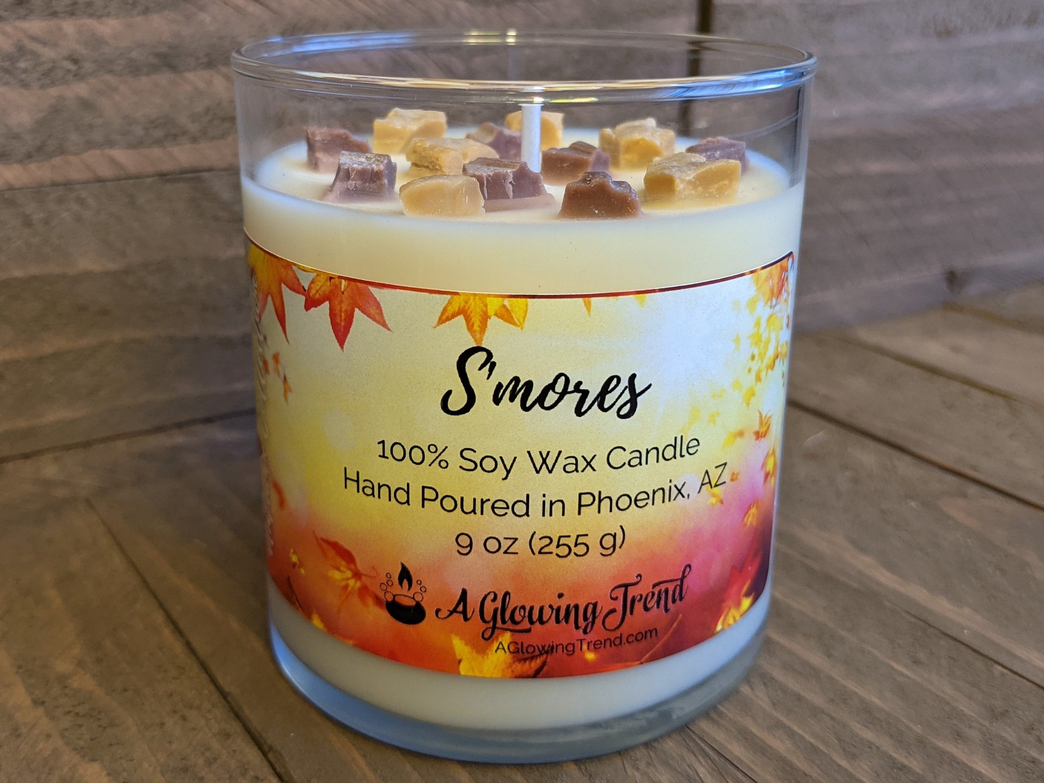 A 9 oz glass tumbler containing a white S'mores scented soy candle topped with wax graham cracker and chocolate bits by A Glowing Trend.