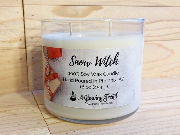 A 16 oz glass tumbler containing a white Snow Witch scented soy candle topped with glitter by A Glowing Trend.