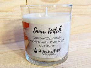 A 9 oz glass tumbler containing a white Snow Witch scented soy candle topped with glitter by A Glowing Trend.