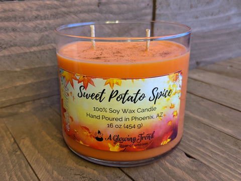 A 16 oz glass tumbler containing an orange Sweet Potato Spice scented soy candle dusted with real cinnamon by A Glowing Trend.