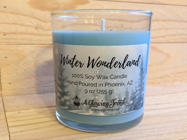 A 9 oz glass tumbler containing a blue Winter Wonderland scented soy candle topped with glitter by A Glowing Trend.